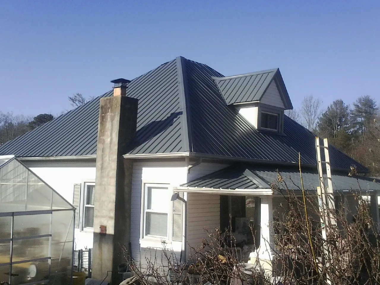 Dark blue standing seam metal roof on a white farmhouse with dormer — Slate & Tile Roof Repair by Roofing Brothers in Vandergrift