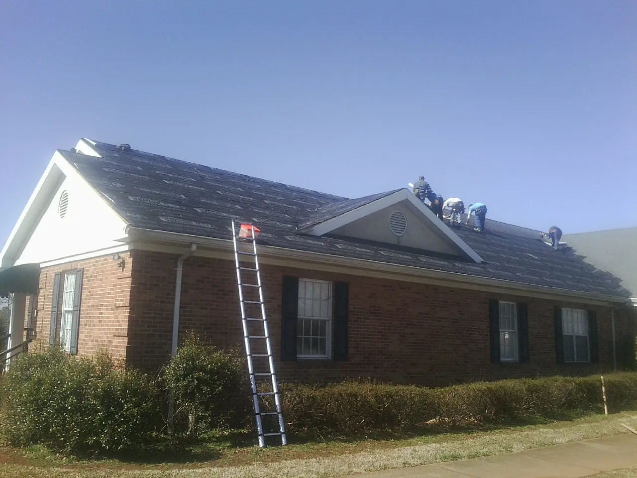 Crew tearing shingles off a brick ranch roof with a ladder set — Metal Roof Repair work by our crew in Vandergrift