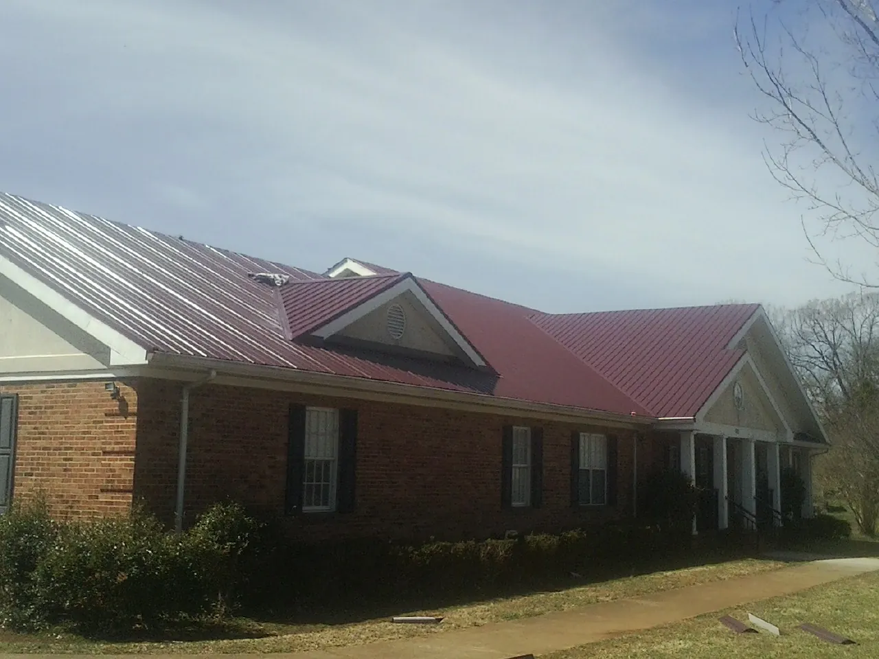 Red metal roof with gabled entries on a long brick building, from a Hail Damage Roof Repair job in Vandergrift