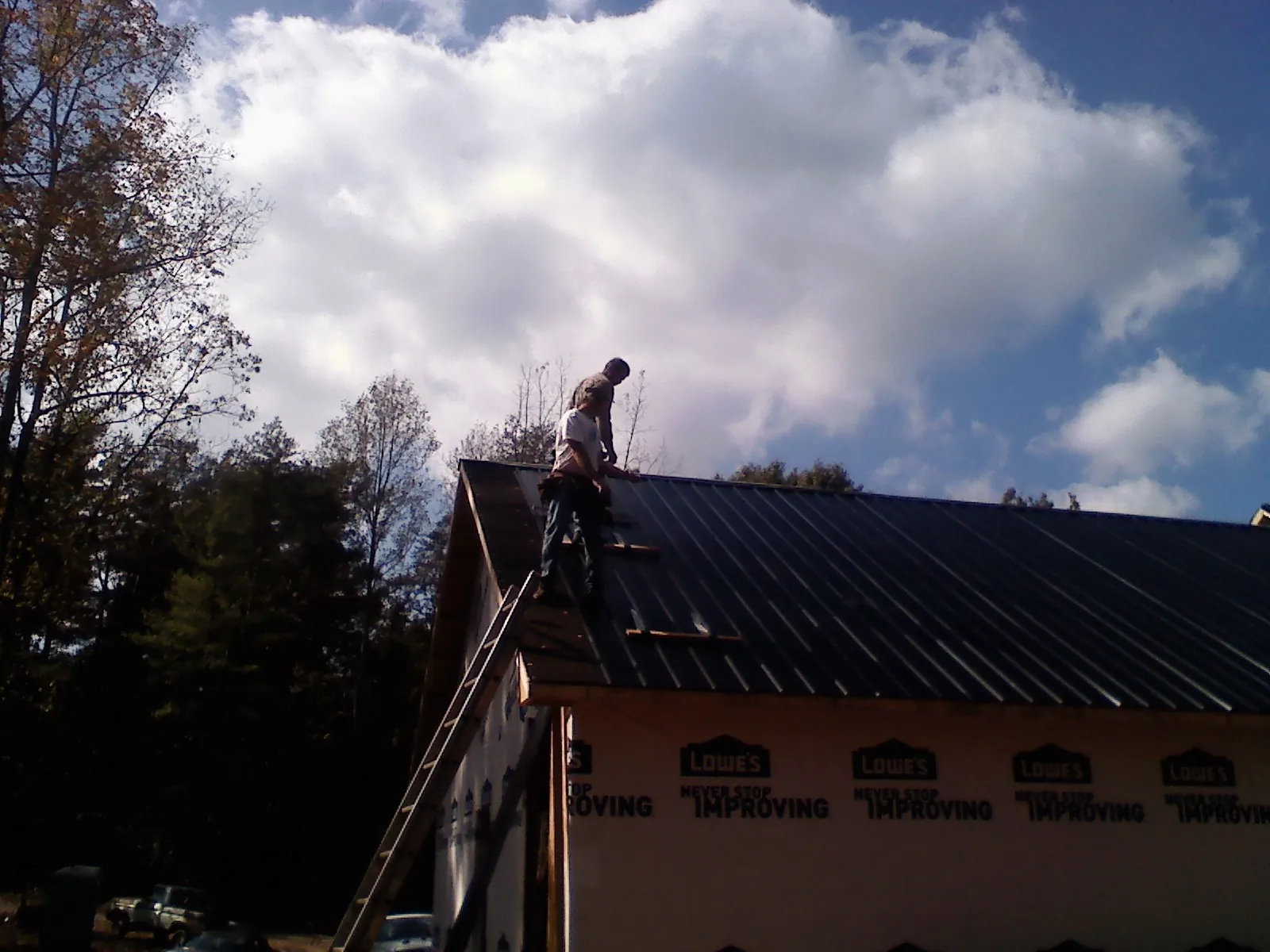 Roofer fastening dark metal panels high against a cloudy sky, from a Roof Inspection job in Vandergrift