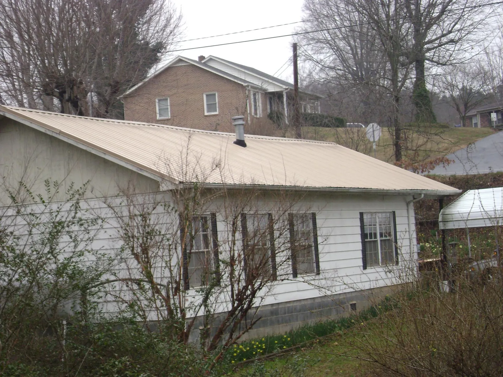 Tan metal roof on a white sided house set into a hillside — Commercial Roofing by Roofing Brothers in Vandergrift